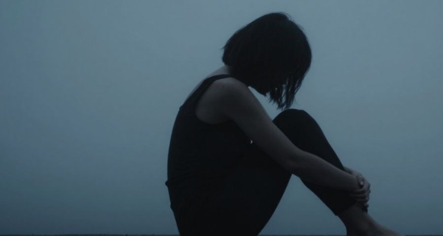 A woman sitting alone in a dimly lit room, chest tight, surrounded by atmospheric fog